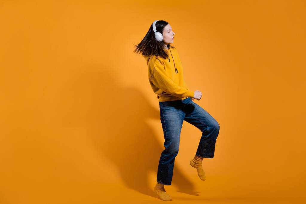 Χαρούμενος λάτρης της μουσικής. Μια νεαρή γυναίκα με κίτρινη κουκούλα με λευκά ασύρματα ακουστικά, - Φωτογραφία, εικόνα