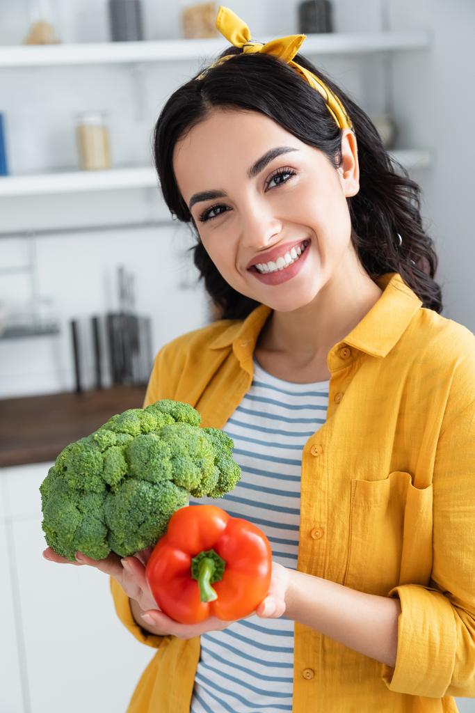 heureuse femme brune tenant brocoli vert mûr et poivron rouge - Photo, image