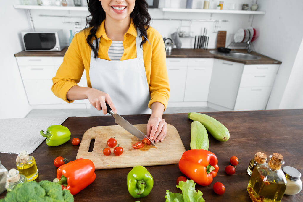 vue recadrée d'une femme joyeuse coupant des tomates cerises sur une planche à découper en bois près des légumes  - Photo, image