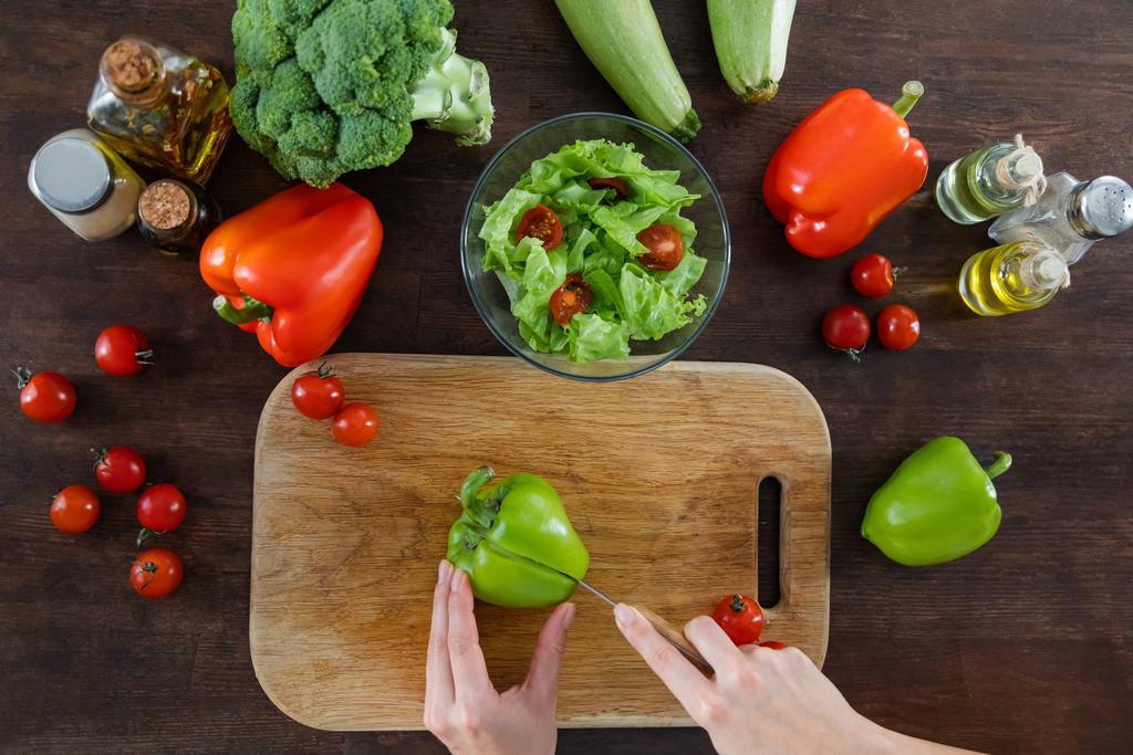 top view of woman cutting fresh bell pepper on wooden chopping board near ripe vegetables  - Photo, Image