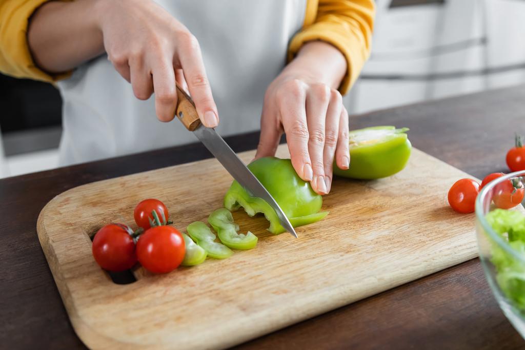 vista recortada de la mujer cortando pimiento verde cerca de tomates cherry en la tabla de cortar  - Foto, Imagen