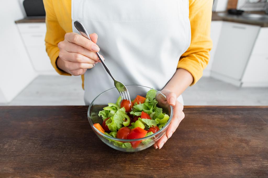 vue recadrée de la jeune femme dans tablier tenant fourchette près de la salade dans un bol - Photo, image