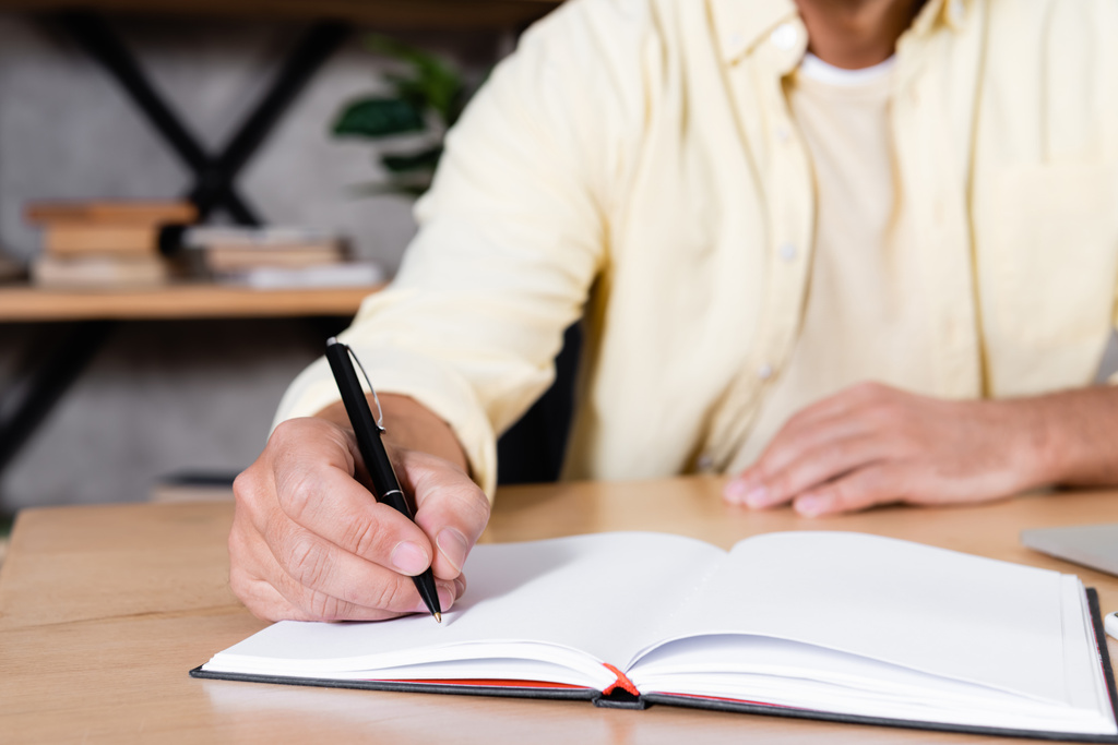gedeeltelijke weergave van de mens schrijven in notebook tijdens het werken thuis, wazig achtergrond - Foto, afbeelding