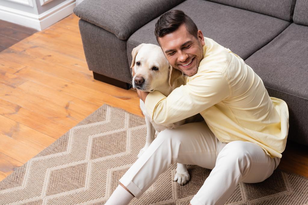 високий кут зору людини з закритими очима, сидячи на підлозі і обіймаючи собаку-лабрадора
 - Фото, зображення