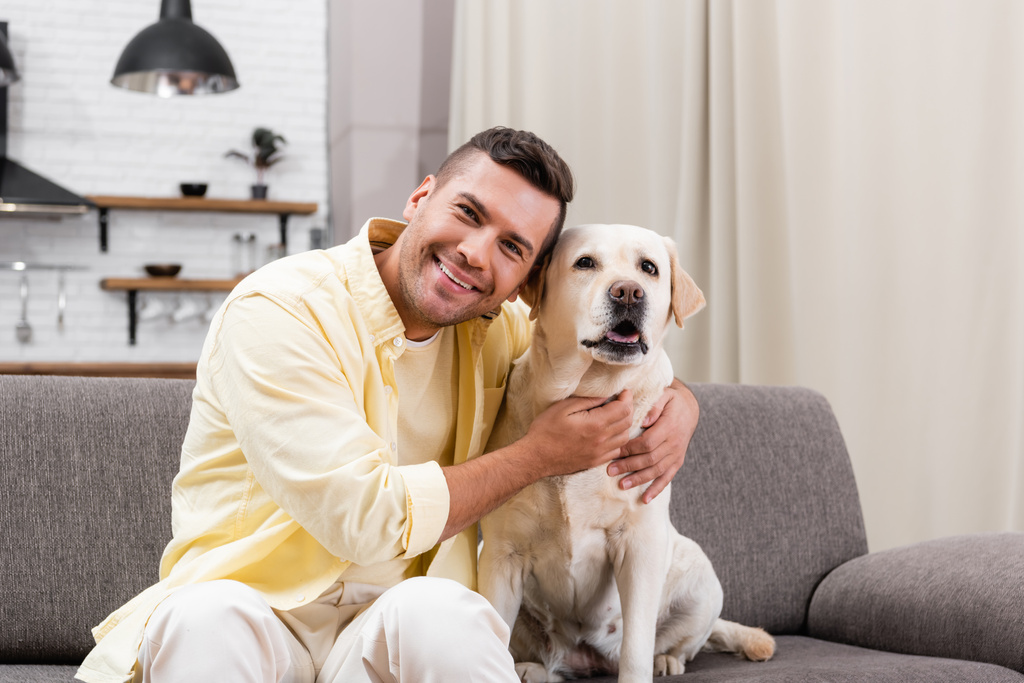 uomo felice sorridente alla macchina fotografica mentre abbraccia cane labrador - Foto, immagini