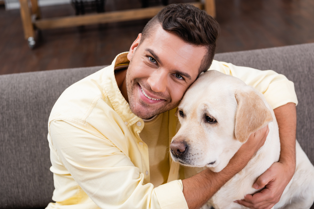 カメラで微笑みながらラブラドール犬を抱きかかえている若い男 - 写真・画像