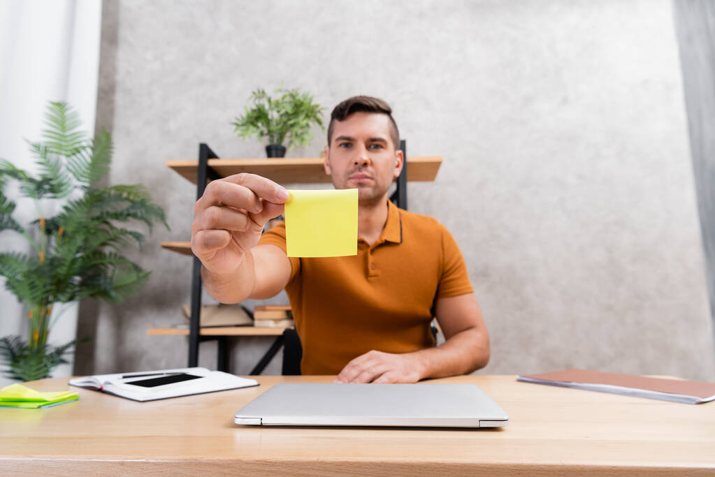 Merkez ofiste oturan serbest çalışan birinin elindeki boş yapışkan notun seçici odağı - Fotoğraf, Görsel
