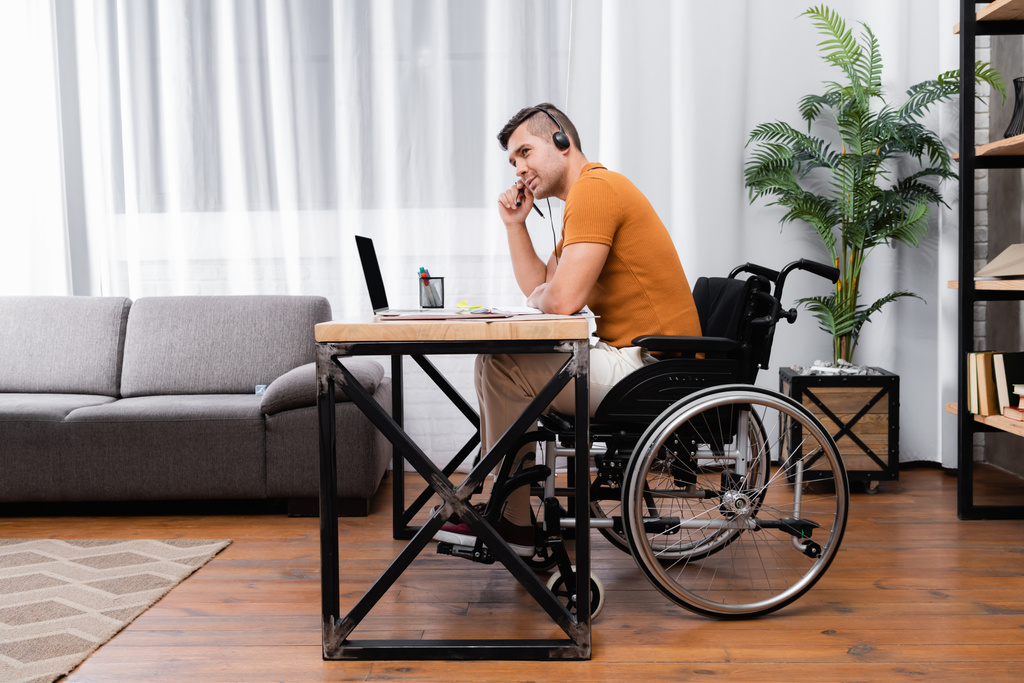 homem com deficiência no fone de ouvido trabalhando perto de laptop em casa - Foto, Imagem