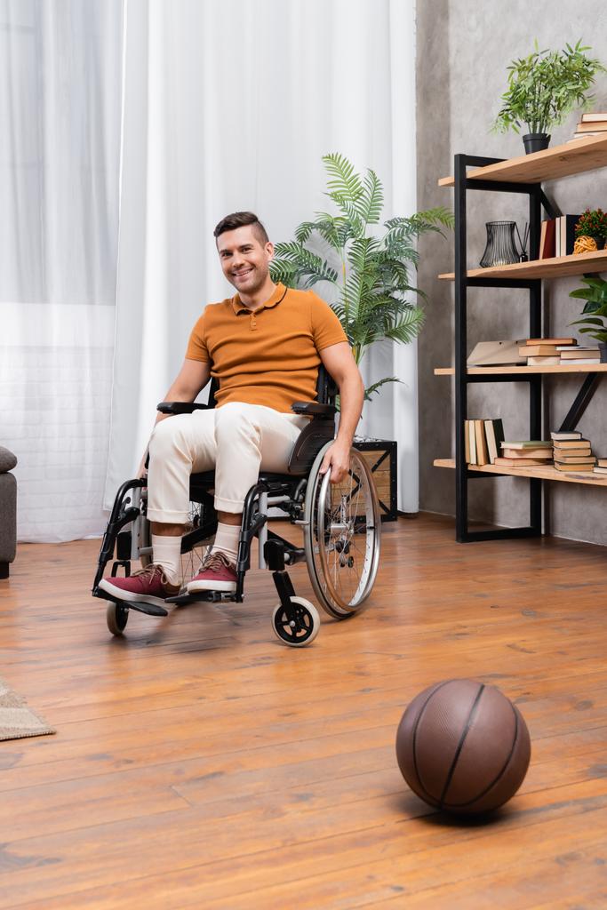 positieve gehandicapte man zit in rolstoel in de buurt van basketbal op de vloer - Foto, afbeelding