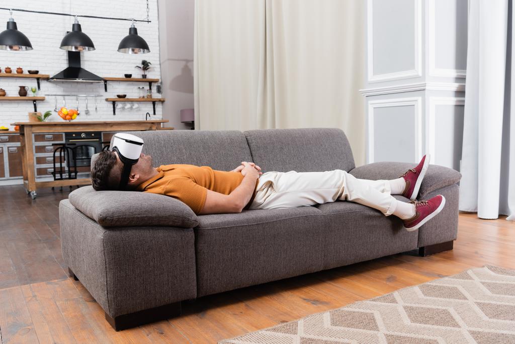 mladý muž v ležérní oblečení relaxační ve vr sluchátka na pohovce doma - Fotografie, Obrázek