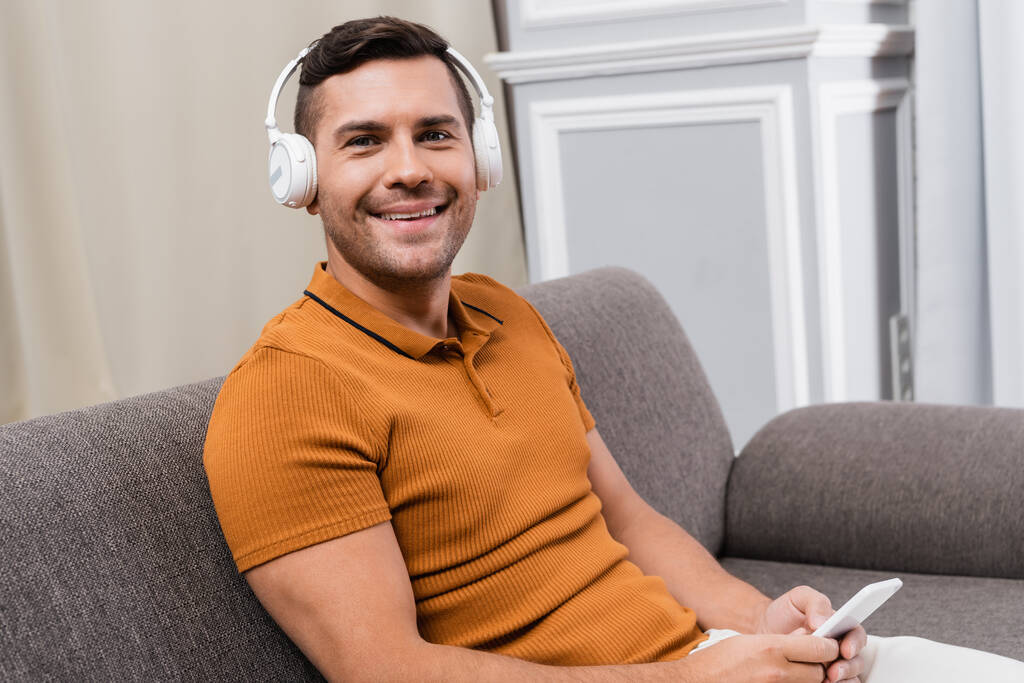 hombre alegre sonriendo a la cámara mientras escucha música en auriculares inalámbricos - Foto, imagen