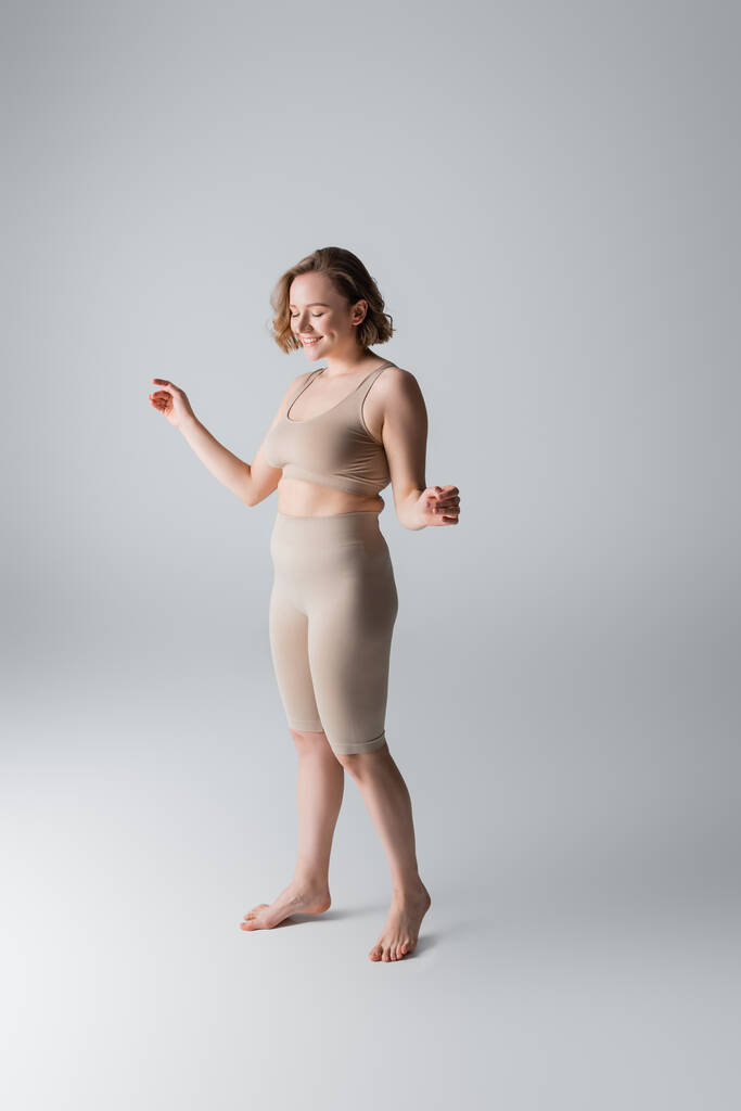 comprimento total de excesso de peso e mulher satisfeita em lingerie posando em cinza - Foto, Imagem