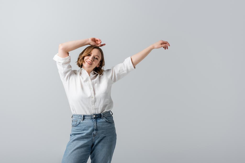 overweight and pleased woman in white shirt posing with hands above head isolated on grey  - Photo, Image