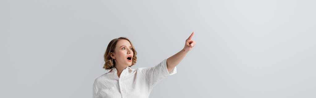Beyaz tişörtlü şişman ve şok olmuş bir kadın, gri pankartta izole edilmiş bir parmakla işaret ediyor. - Fotoğraf, Görsel
