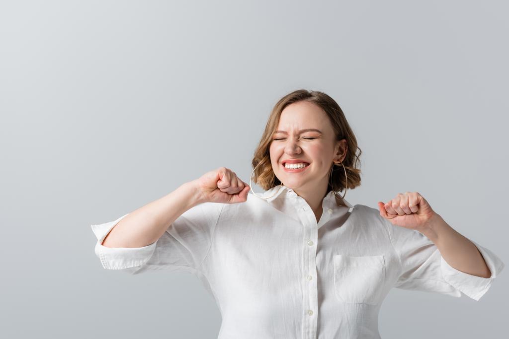 tevreden overgewicht vrouw in wit shirt vieren geïsoleerd op grijs  - Foto, afbeelding