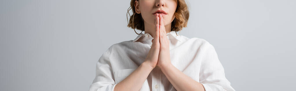 vista recortada de mujer joven con sobrepeso en camisa blanca con las manos de oración aisladas en gris, pancarta - Foto, imagen