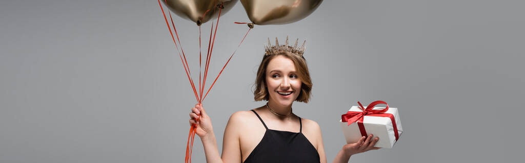happy plus size woman in slip dress and crown holding golden balloons and present isolated on grey, banner - Photo, Image