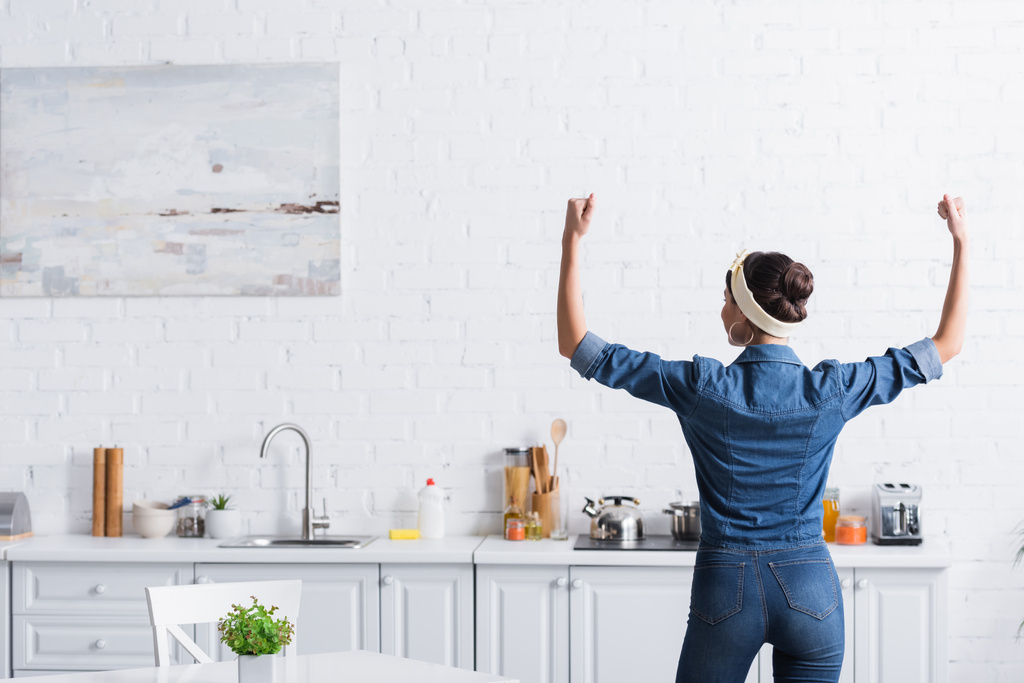 Vista posterior de ama de casa en camisa de mezclilla mostrando los músculos en la cocina  - Foto, Imagen