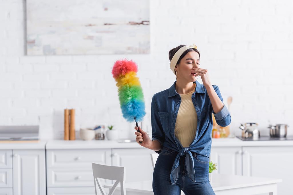 Ama de casa con cepillo de polvo estornudando en la cocina  - Foto, Imagen