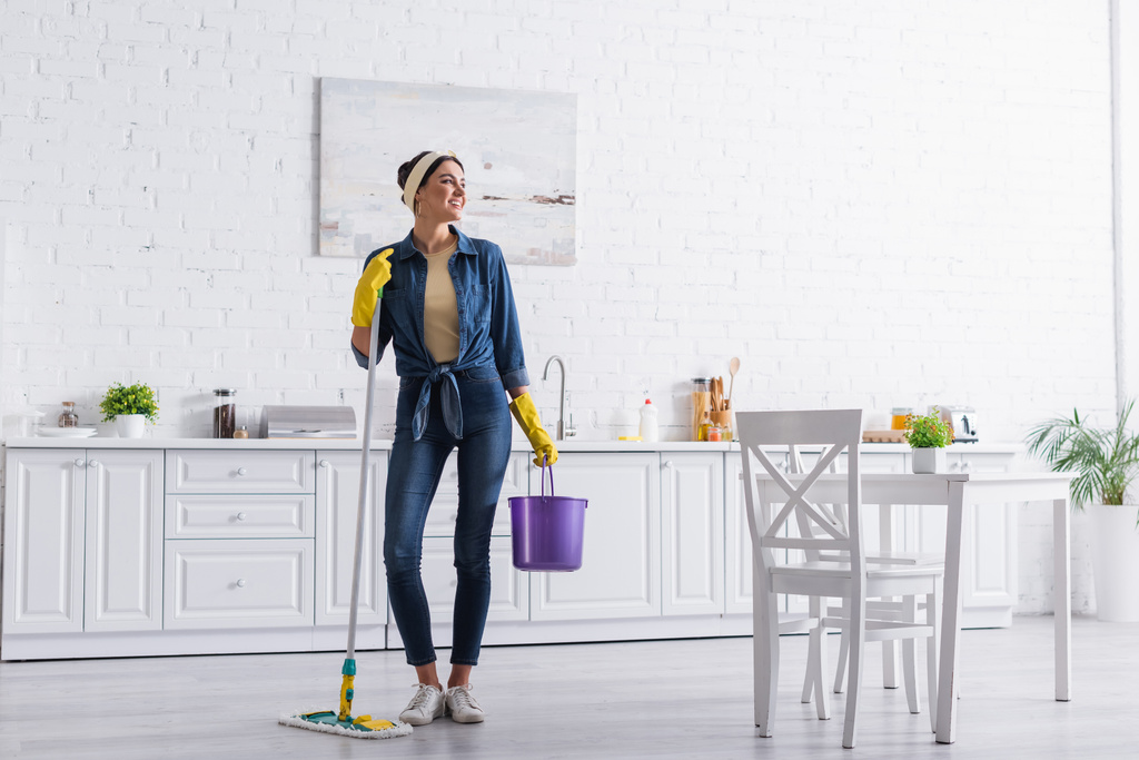Позитивна домогосподарка тримає відро і мопед на кухні
  - Фото, зображення