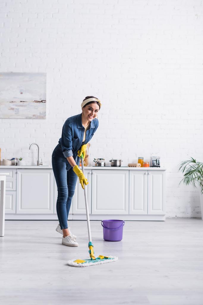 Glückliche Hausfrau putzt Fußboden mit Wischmopp in Küche  - Foto, Bild