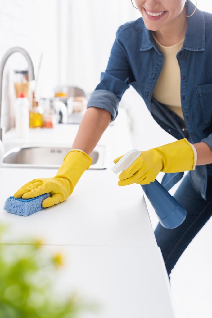 Oříznutý pohled na usmívající se žena čištění kuchyňské pracovní desky s pracím práškem a houbou  - Fotografie, Obrázek