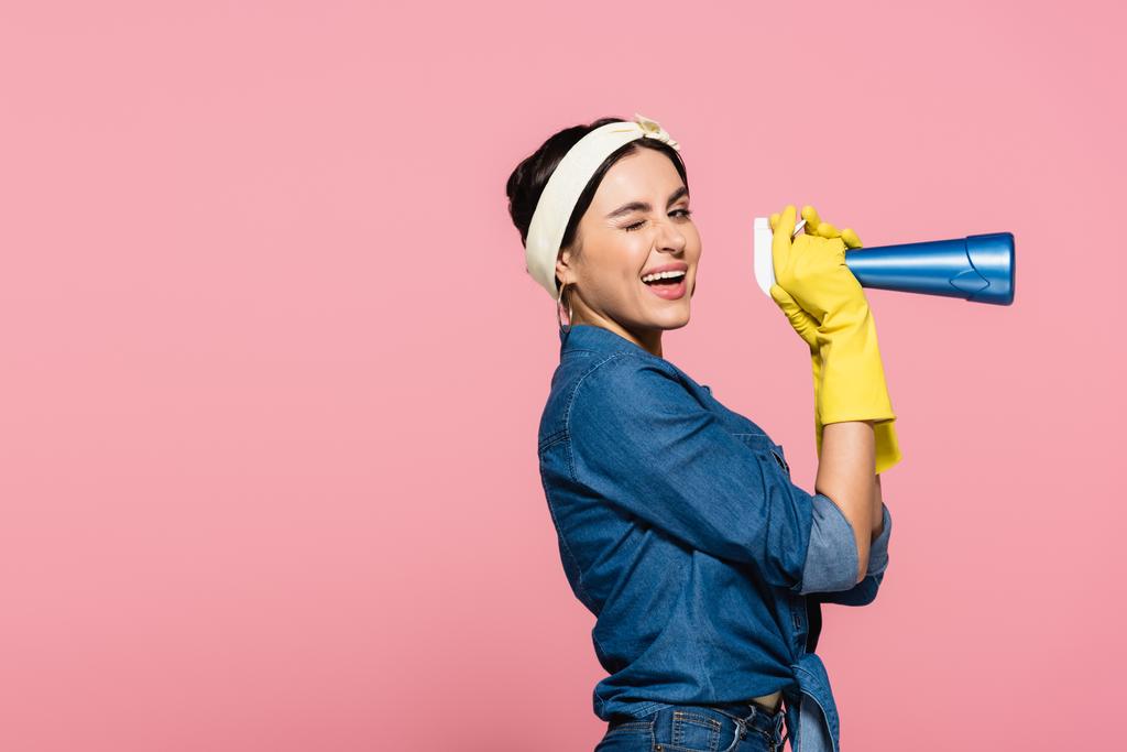 Lächelnde Hausfrau in Gummihandschuhen hält Waschmittel in der Hand und zwinkert vereinzelt in die Kamera - Foto, Bild