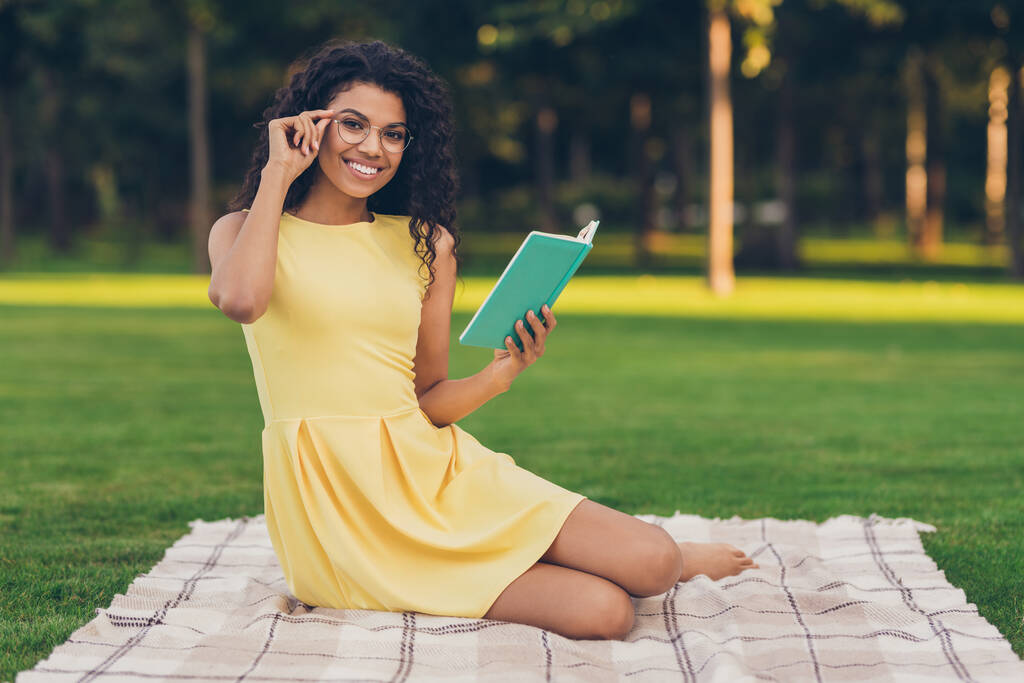 Portrait of attractive smart cheerful girl sitting on duvet reading interesting book free time studying on fresh air outdoor - Photo, Image