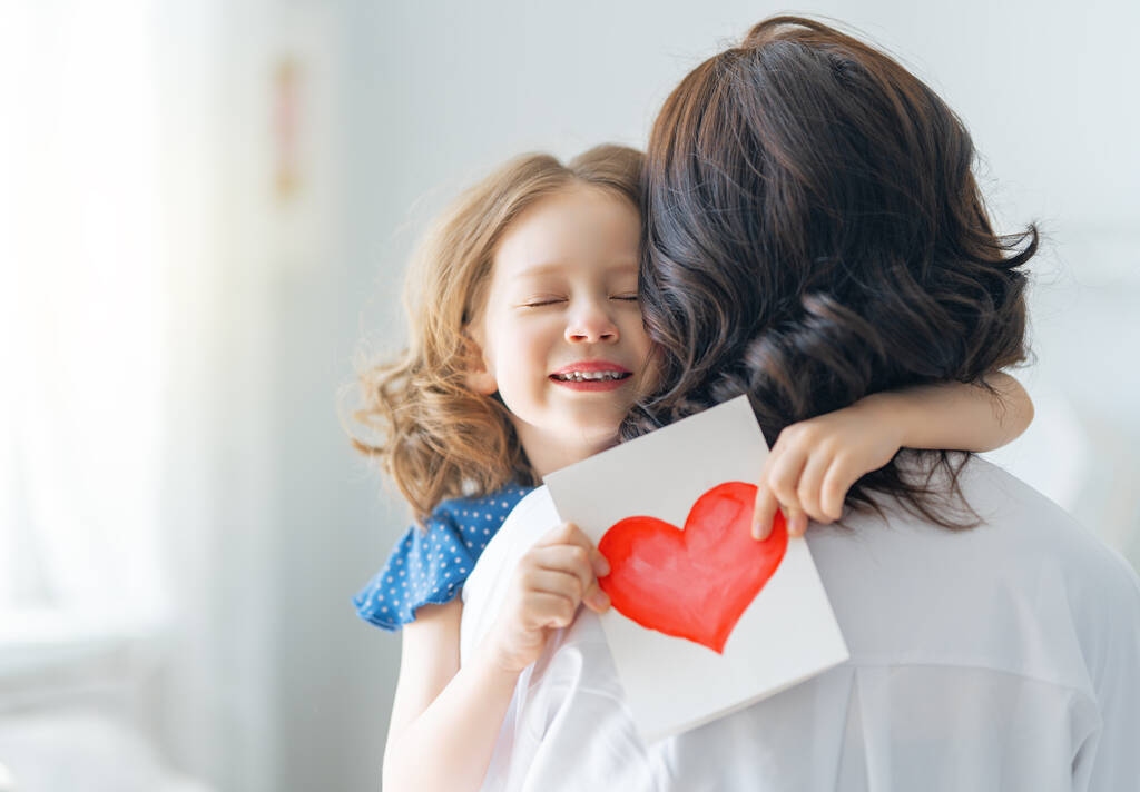 Alles Gute zum Muttertag! Die Tochter gratuliert der Mutter und überreicht ihr eine Postkarte. Mutter und Mädchen lächeln und umarmen sich. Familienurlaub und Zweisamkeit. - Foto, Bild