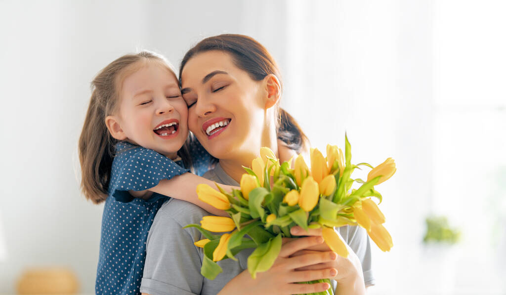 Anneler Günün kutlu olsun. Çocuk kızı annesini tebrik eder ve ona çiçek verir. Anne ve kız gülümsüyor ve sarılıyorlar. Aile tatili ve birliktelik. - Fotoğraf, Görsel