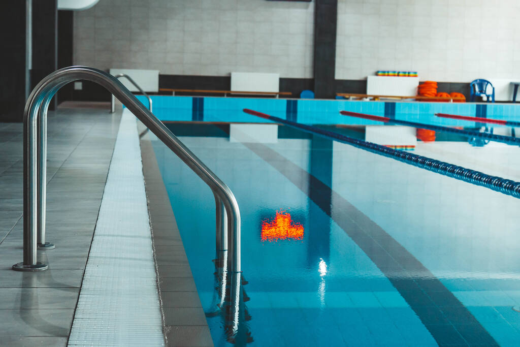 una piscina de agua con agua transparente azul, sobre la que brilla la luz del sol. Carriles de agua en la piscina. campo de deportes de interior para nadar. - Foto, Imagen