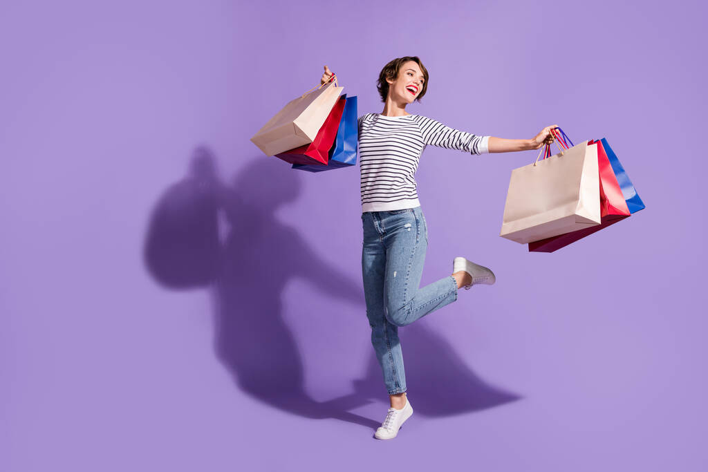 Täyspitkä kuva makea ostaja nainen pukeutua rento asu tanssia tilalla värikäs ostoskassit eristetty violetti väri tausta - Valokuva, kuva
