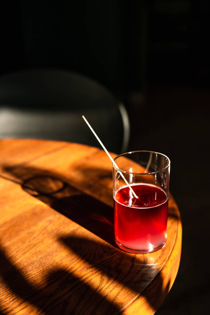 Сладкий и кислый освежающий коктейль из ежевичного джина с ежевикой в бокале хайбол без льда в прямом солнечном свете с длинными тенями, на деревянном столе - Фото, изображение