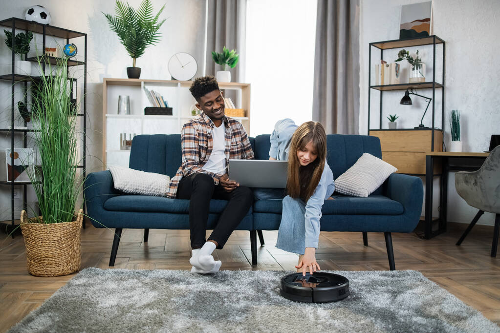 Laptopot és robotporszívót használó házaspár háztartási használatra - Fotó, kép