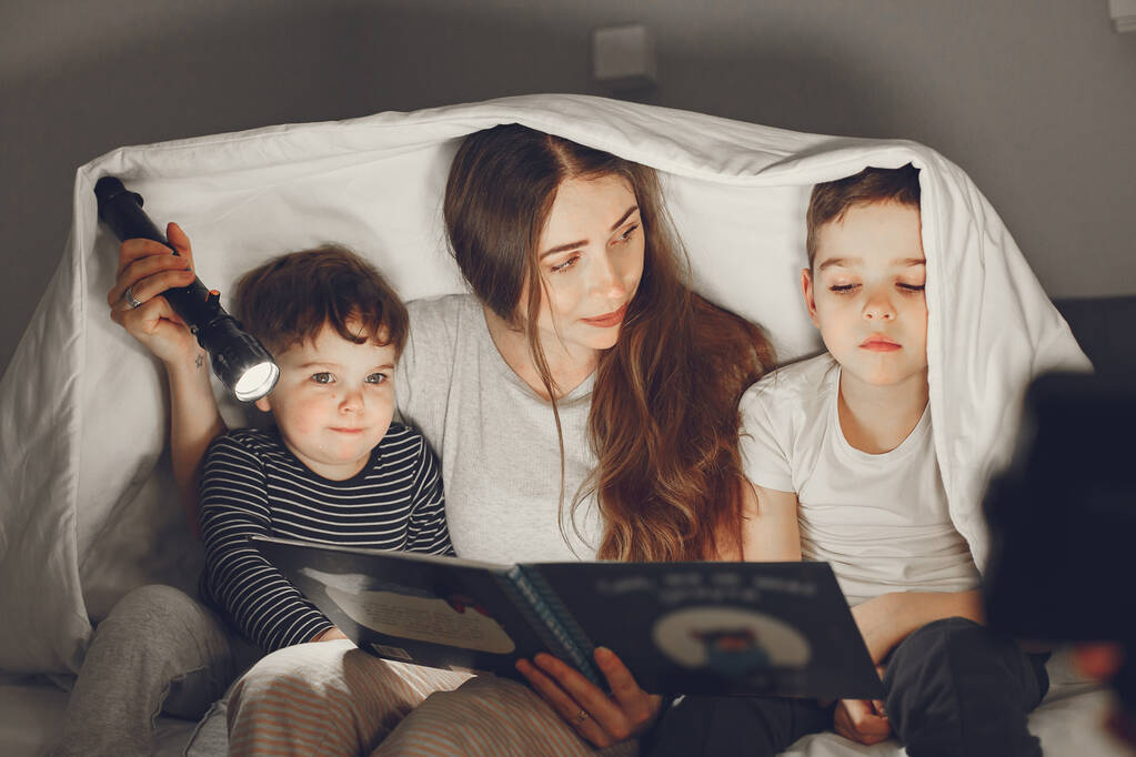 Mama i dziecko czytają książkę z latarką - Zdjęcie, obraz