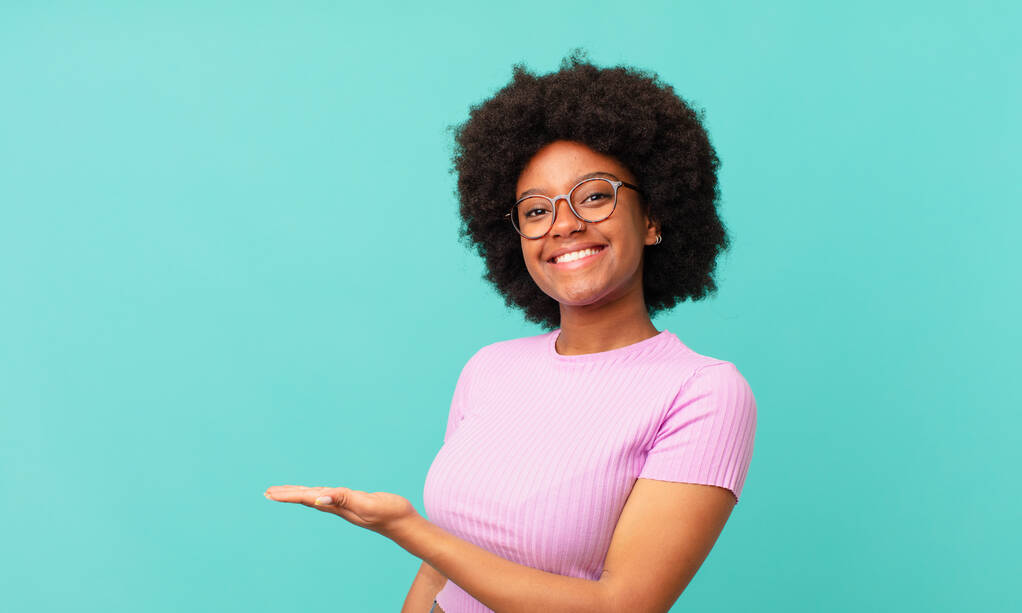 афро-черная женщина улыбается весело, чувствуя себя счастливым и показывая концепцию в копировальном пространстве с ладонью руки - Фото, изображение
