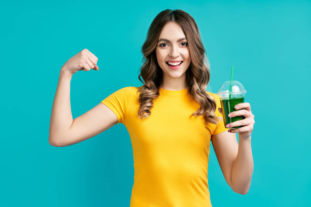 Mulher muito jovem segurando suco de smoothie vegetal desintoxicação verde e mostra músculos - Foto, Imagem