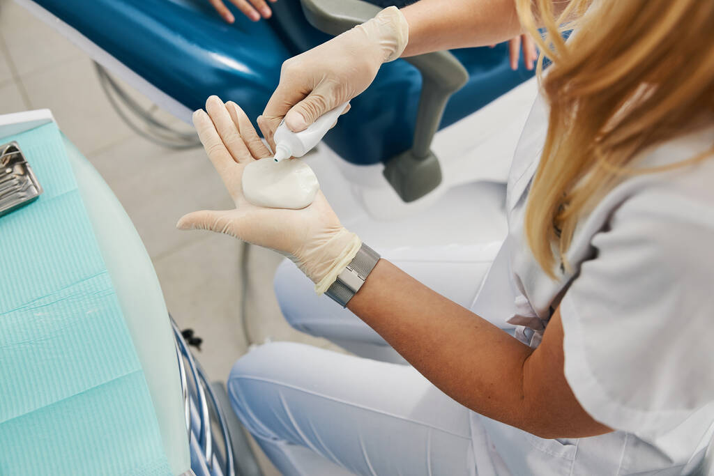 Жінка-стоматолог наливає рідину на кульку шпаклівки для враження щелепи
 - Фото, зображення