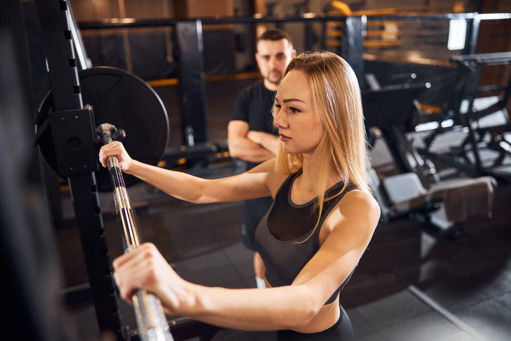 Dama trabajadora haciendo ejercicio en el gimnasio con la ayuda del entrenador - Foto, imagen