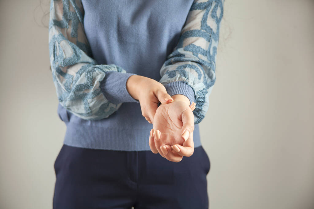 mladá žena ruka v bolesti zápěstí na šedém pozadí - Fotografie, Obrázek