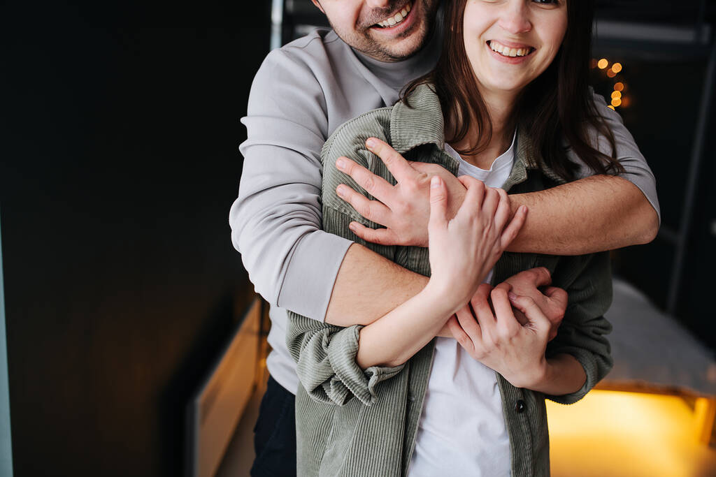 Mutlu bir çiftin kırpılmış görüntüsü. Adam kadına arkadan sarılıyor. Kapat, yarım yüz, bulanık arkaplan. - Fotoğraf, Görsel