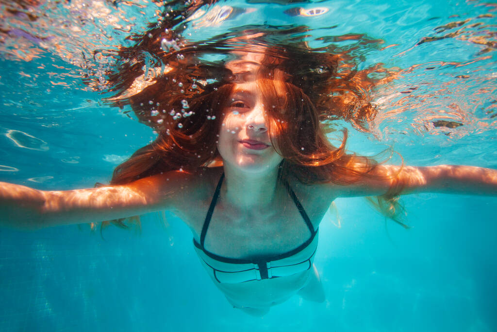 Kaunis vedenalainen muotokuva hymyilevä pieni tyttö, jolla on pitkät inkiväärikarvat - Valokuva, kuva