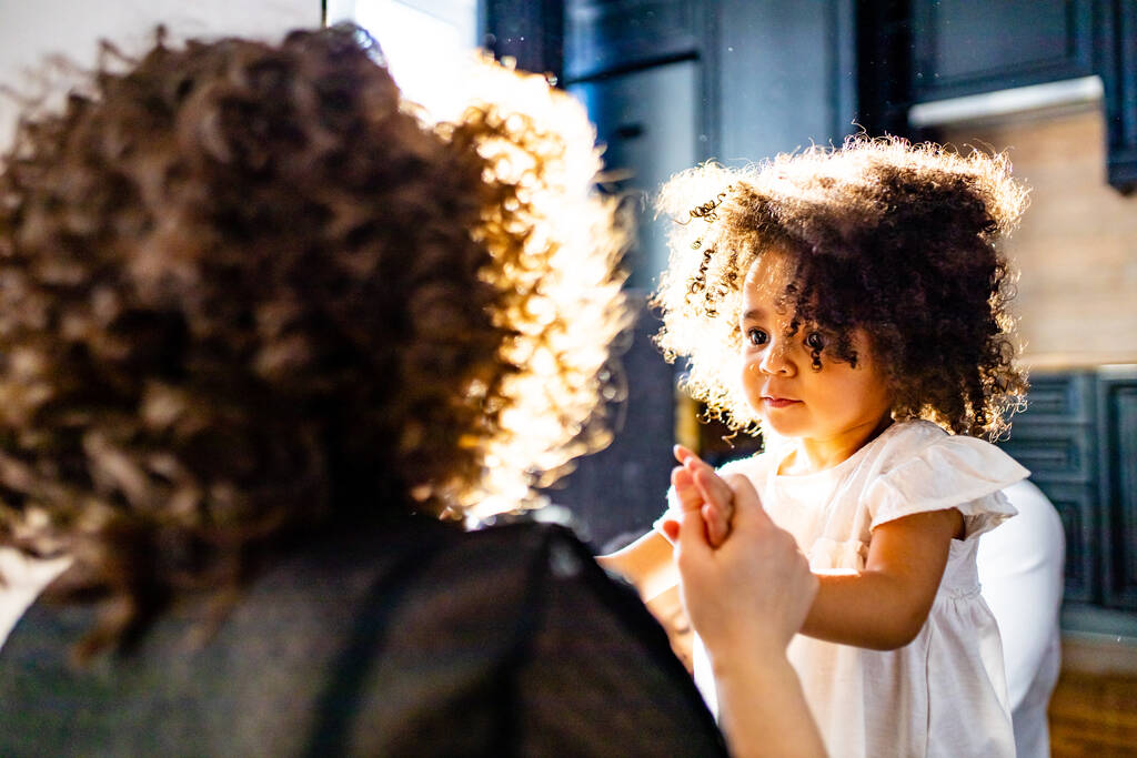 pelo rizado lindo bebé de raza mixta en las manos de las madres en la acogedora sala de luz del día - Foto, Imagen