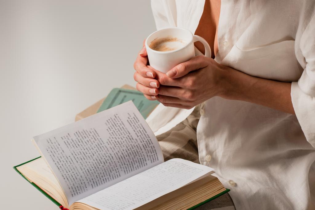 Kitap okuyan ve elinde beyaz bir fincan kahve tutan genç bir kadın.  - Fotoğraf, Görsel