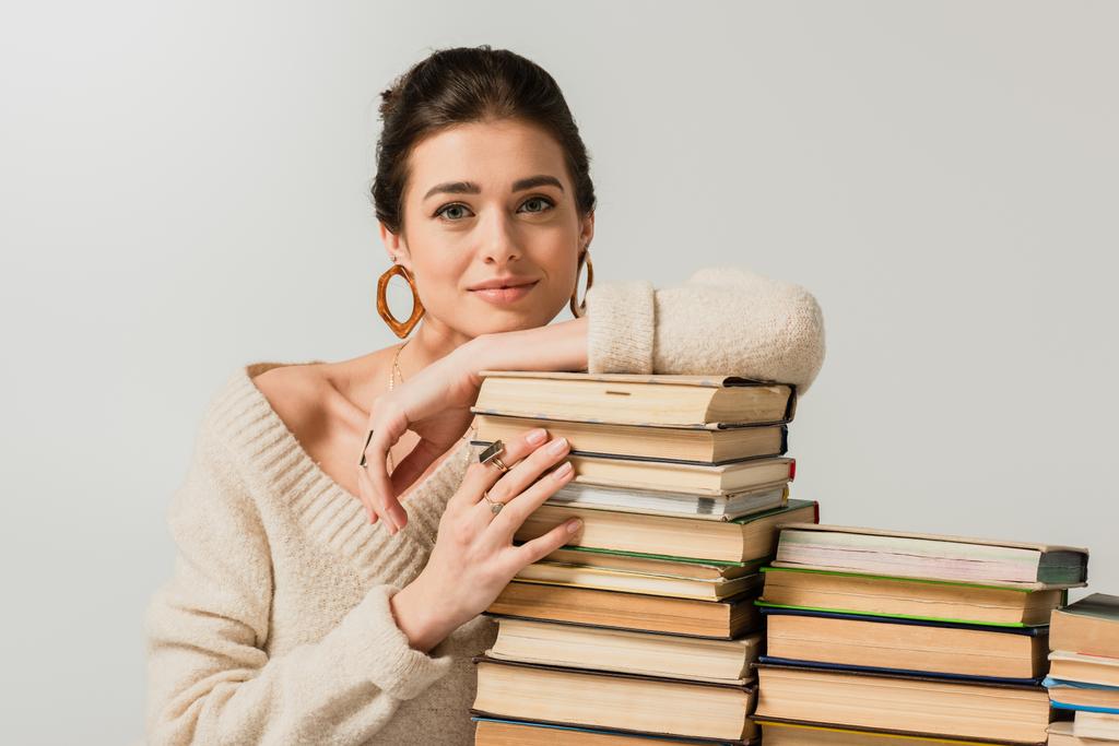 Küpeli genç bir kadın beyaz kitaplara yaslanıyor. - Fotoğraf, Görsel