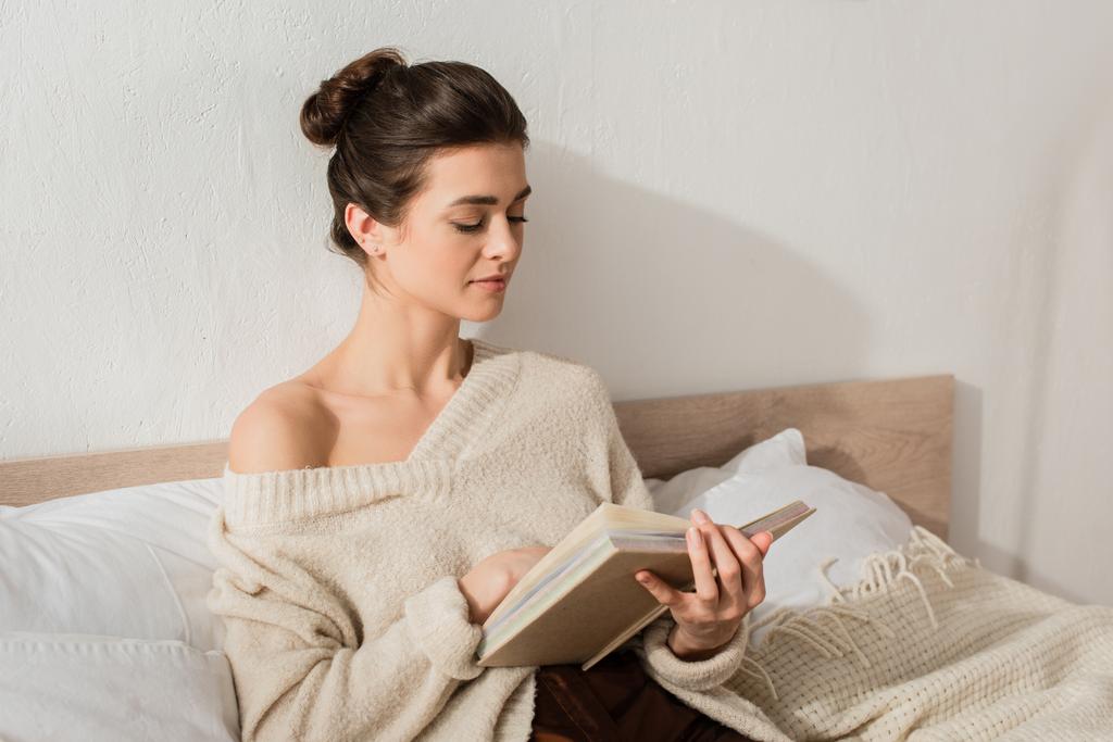 brunette nuori nainen lukeminen kirja, kun lepää sängyssä kotona - Valokuva, kuva