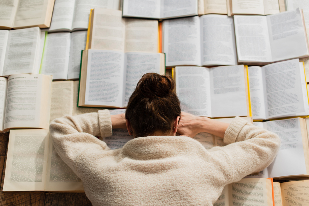κορυφαία άποψη της κουρασμένης γυναίκας που κοιμάται κοντά σε ανοιχτά βιβλία  - Φωτογραφία, εικόνα