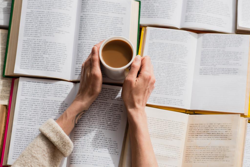 vista parziale della donna che tiene una tazza di caffè vicino a libri aperti  - Foto, immagini