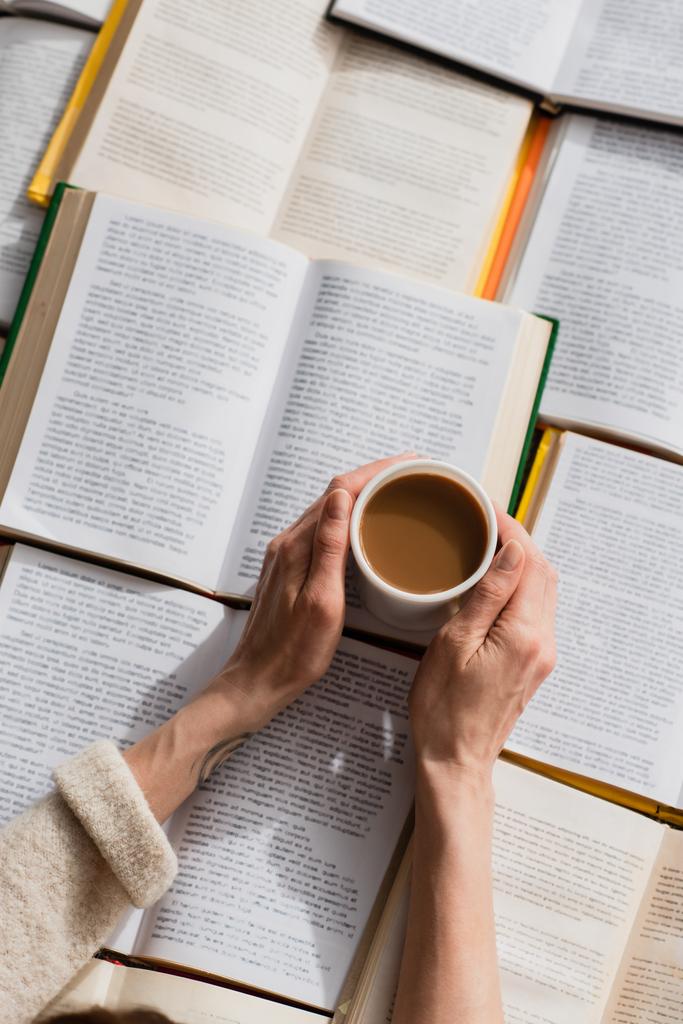 Açık kitapların yanında elinde kahve fincanı olan bir kadın.  - Fotoğraf, Görsel