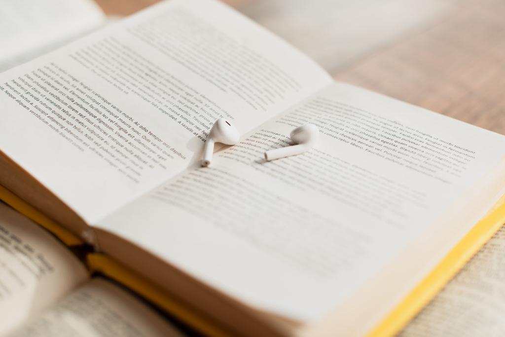 weiße und drahtlose Kopfhörer auf verschwommenem Buch - Foto, Bild